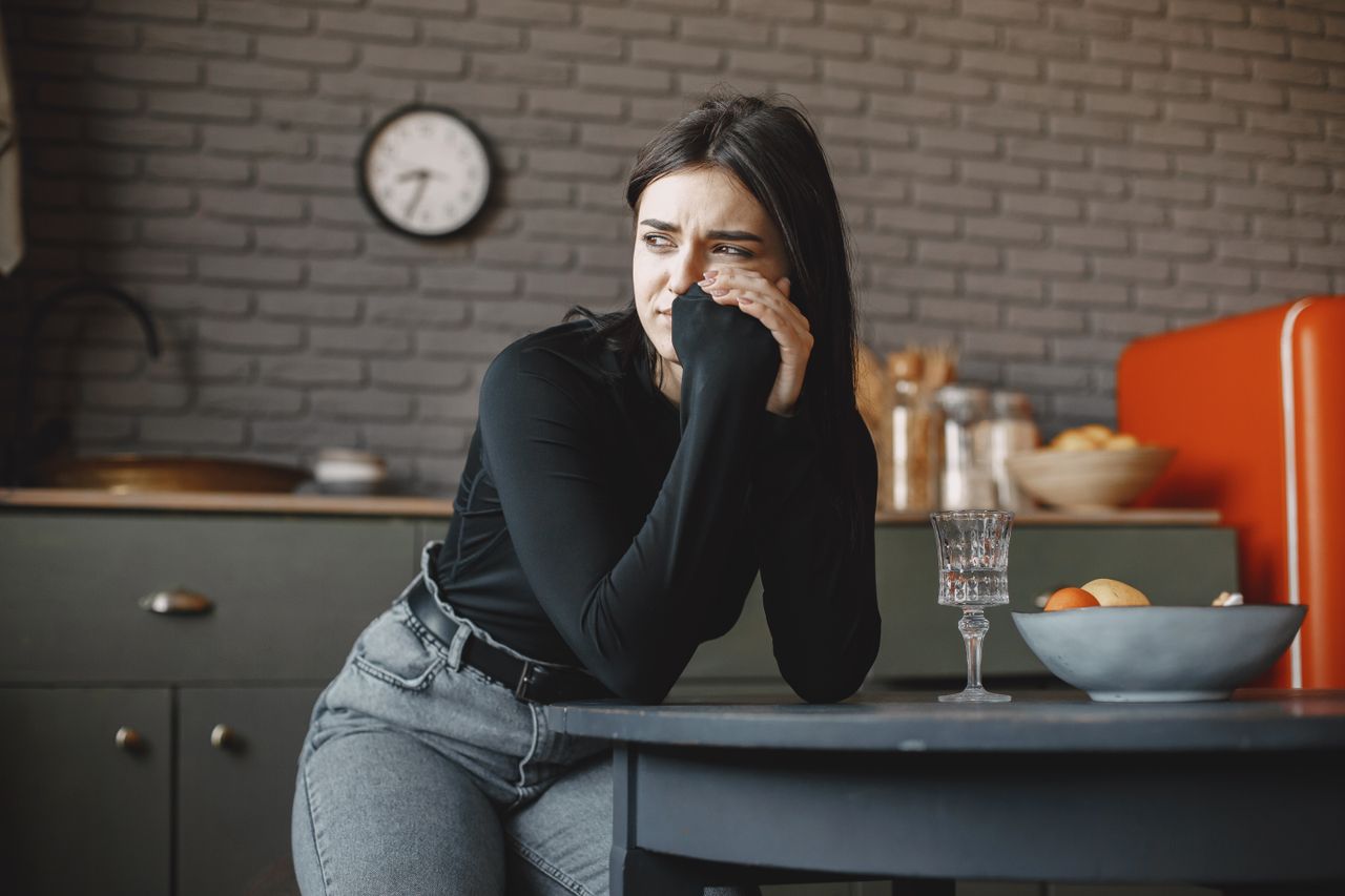 Young woman in a pensive mood, sitting indoors with a clock in the background.